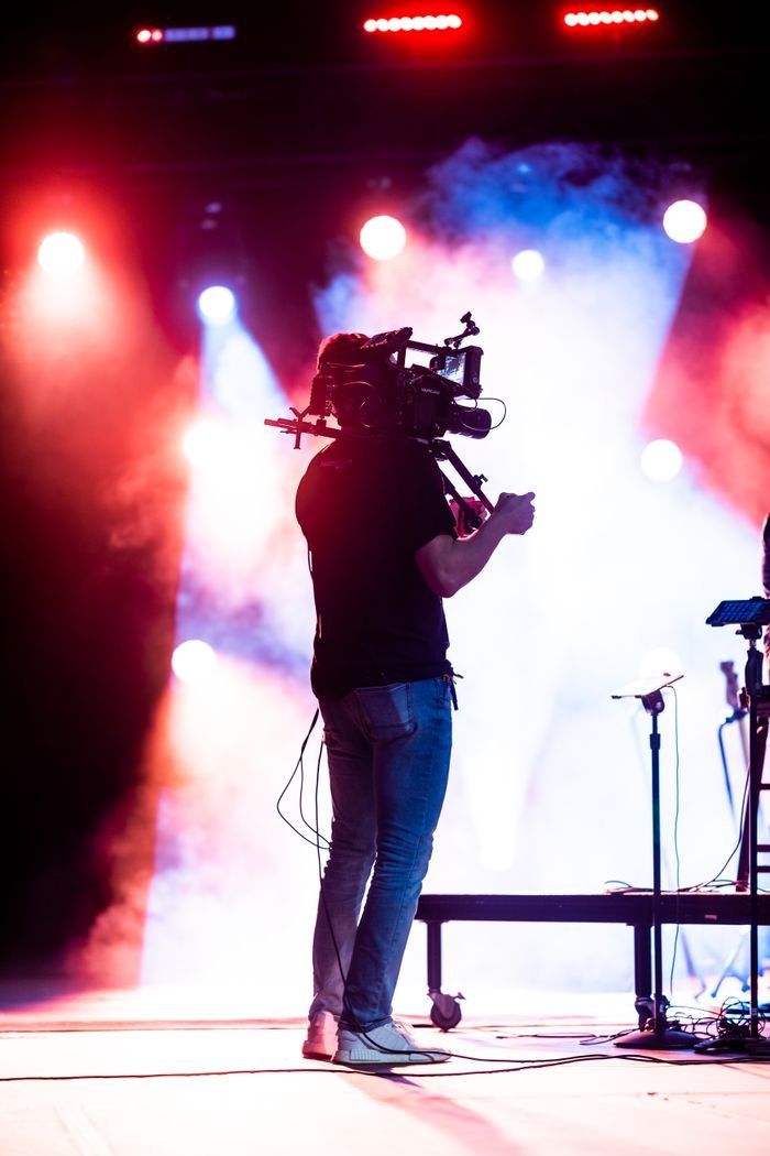 Cameraman operating video camera amidst dramatic stage lighting and fog.
